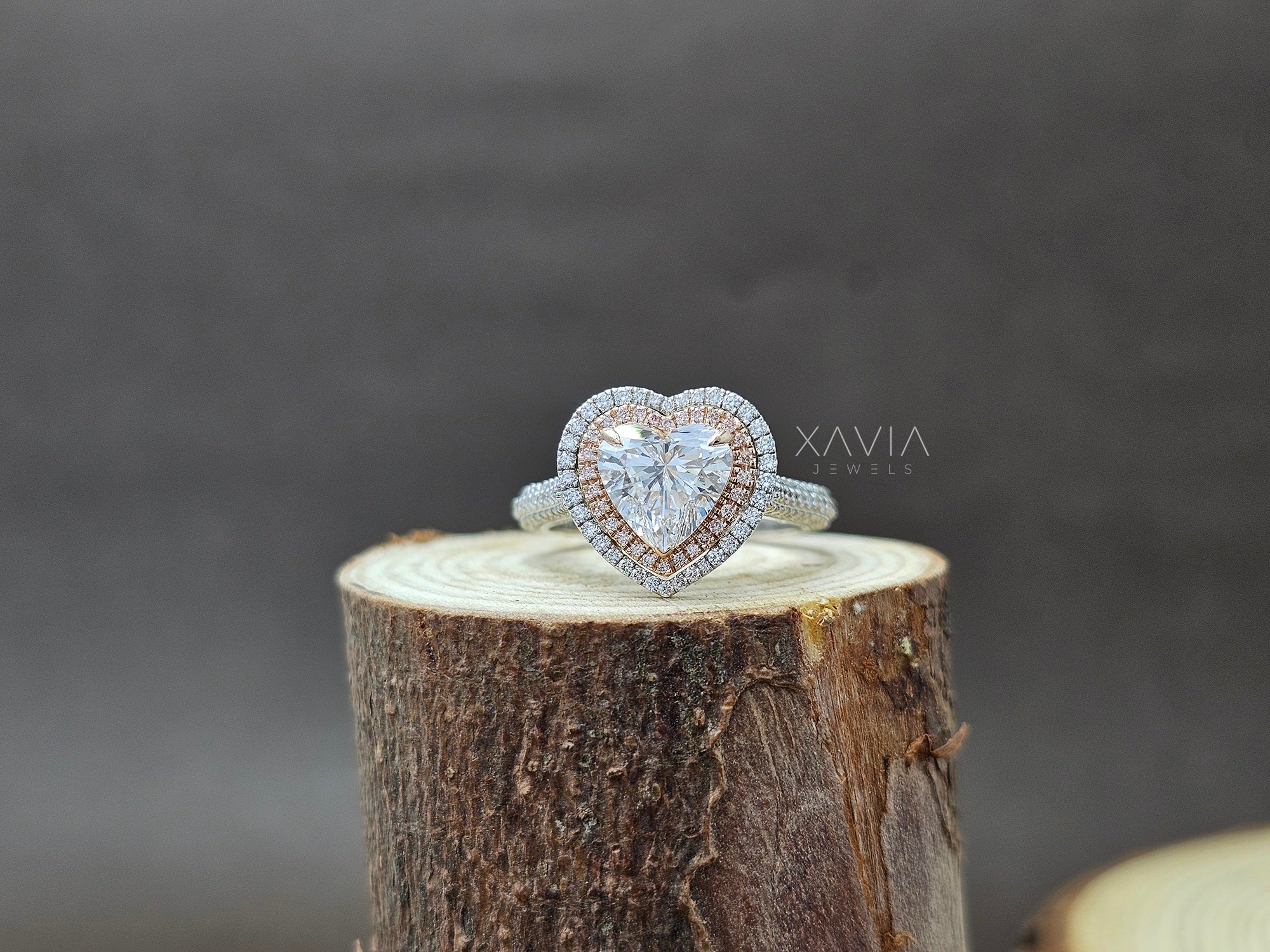Heart-shaped diamond ring on a wooden stump with Xavia Jewels branding.