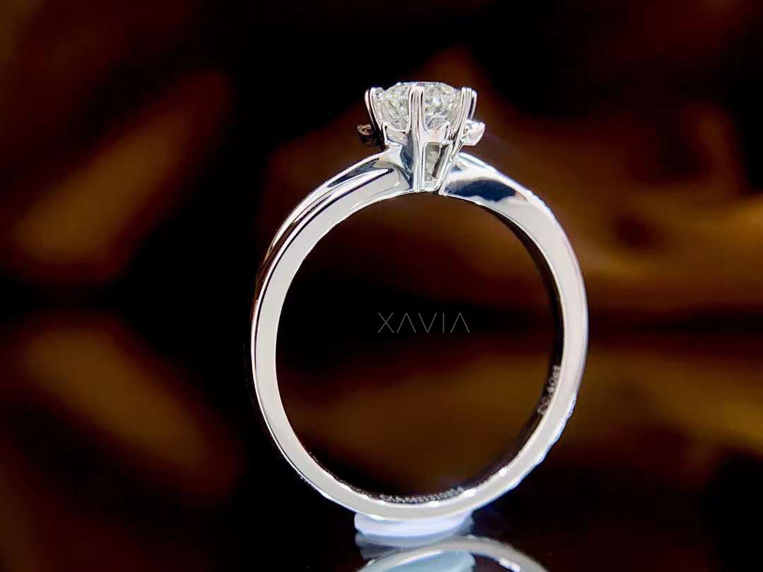 Silver ring with a diamond on a dark background, featuring the brand 'Xavia'.