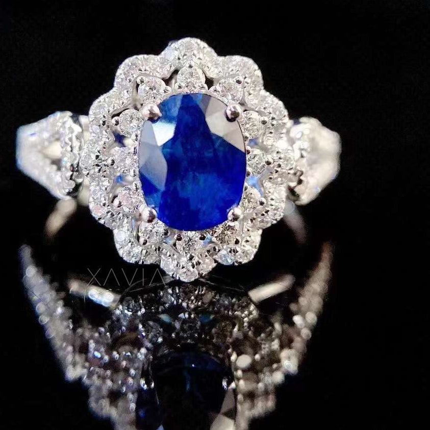 Front view of oval blue sapphire engagement ring with brilliant diamond floral halo and pavé split shank band reflecting luxury fine jewelry design
