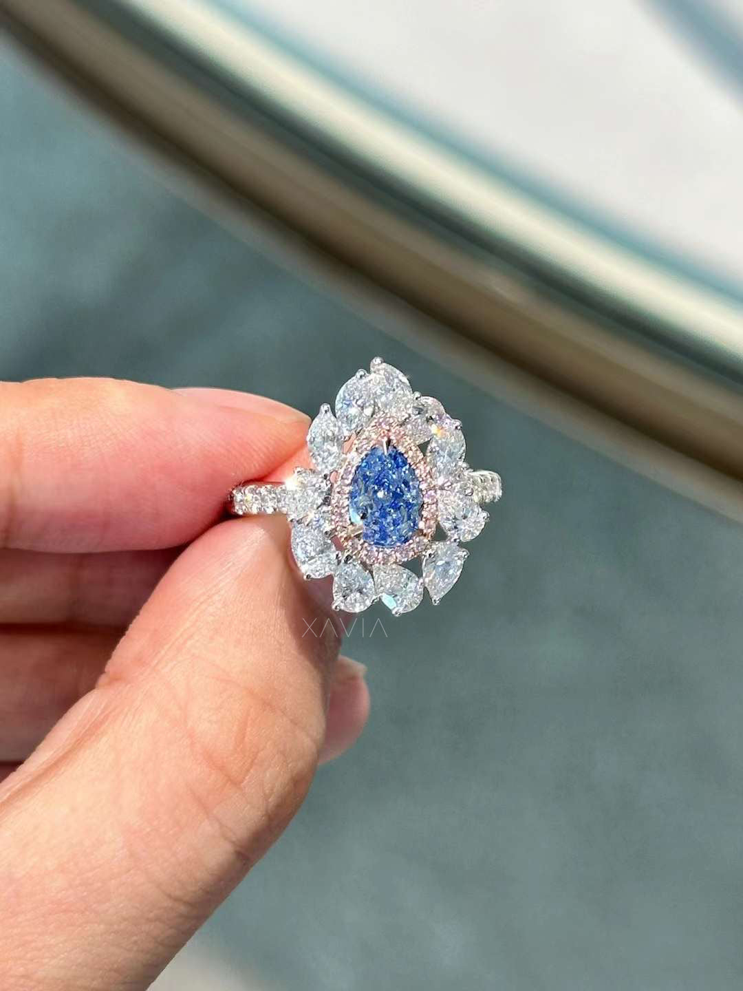 Pear cut blue lab diamond ring with floral marquise halo, pavé band, worn on hand in natural light
