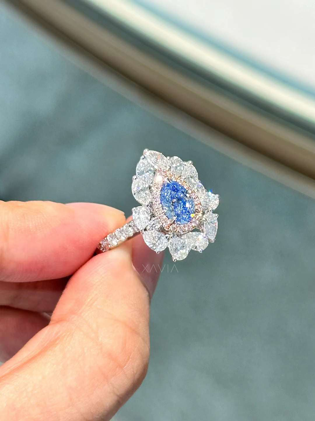 Side profile view of pear shape blue diamond ring with clustered marquise and round halo in platinum
