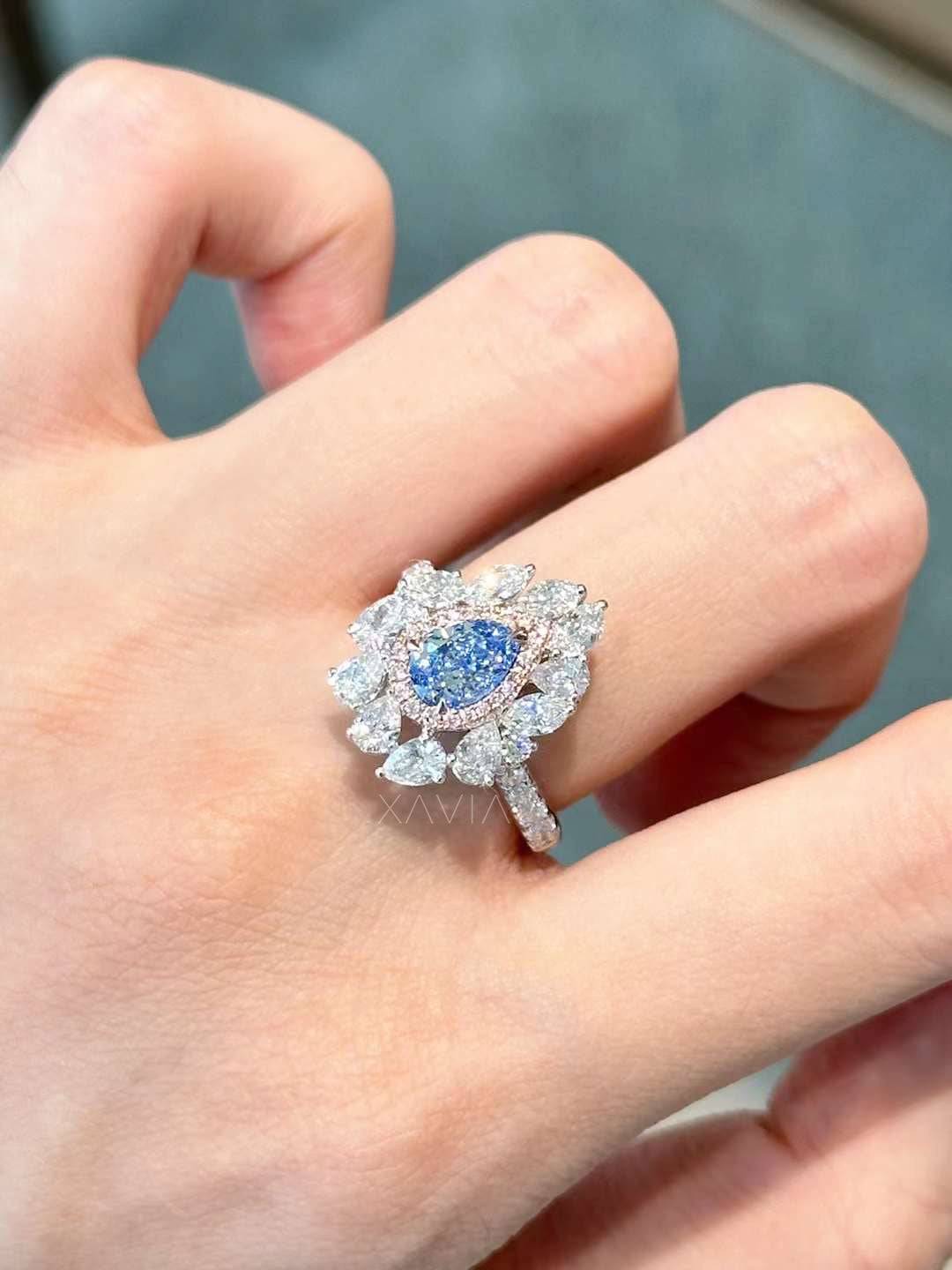 Angled view of pear blue diamond floral halo engagement ring with pavé band in white gold