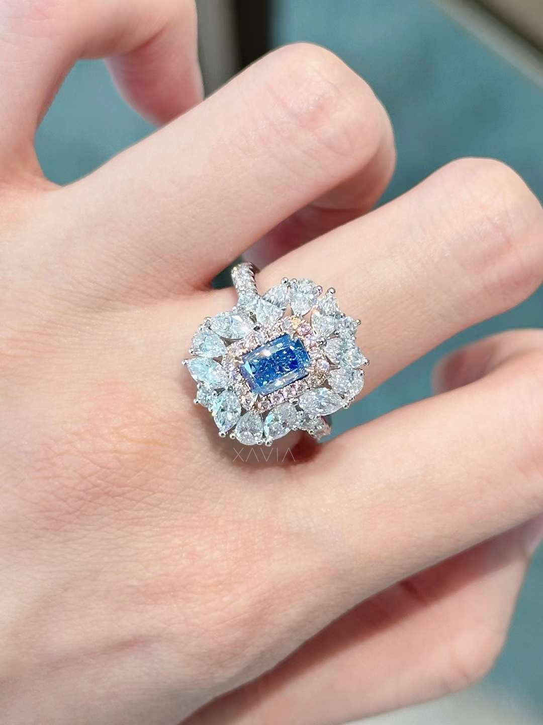 blue emerald cut halo diamond ring worn on hand showcasing marquise diamond burst and pavé band
