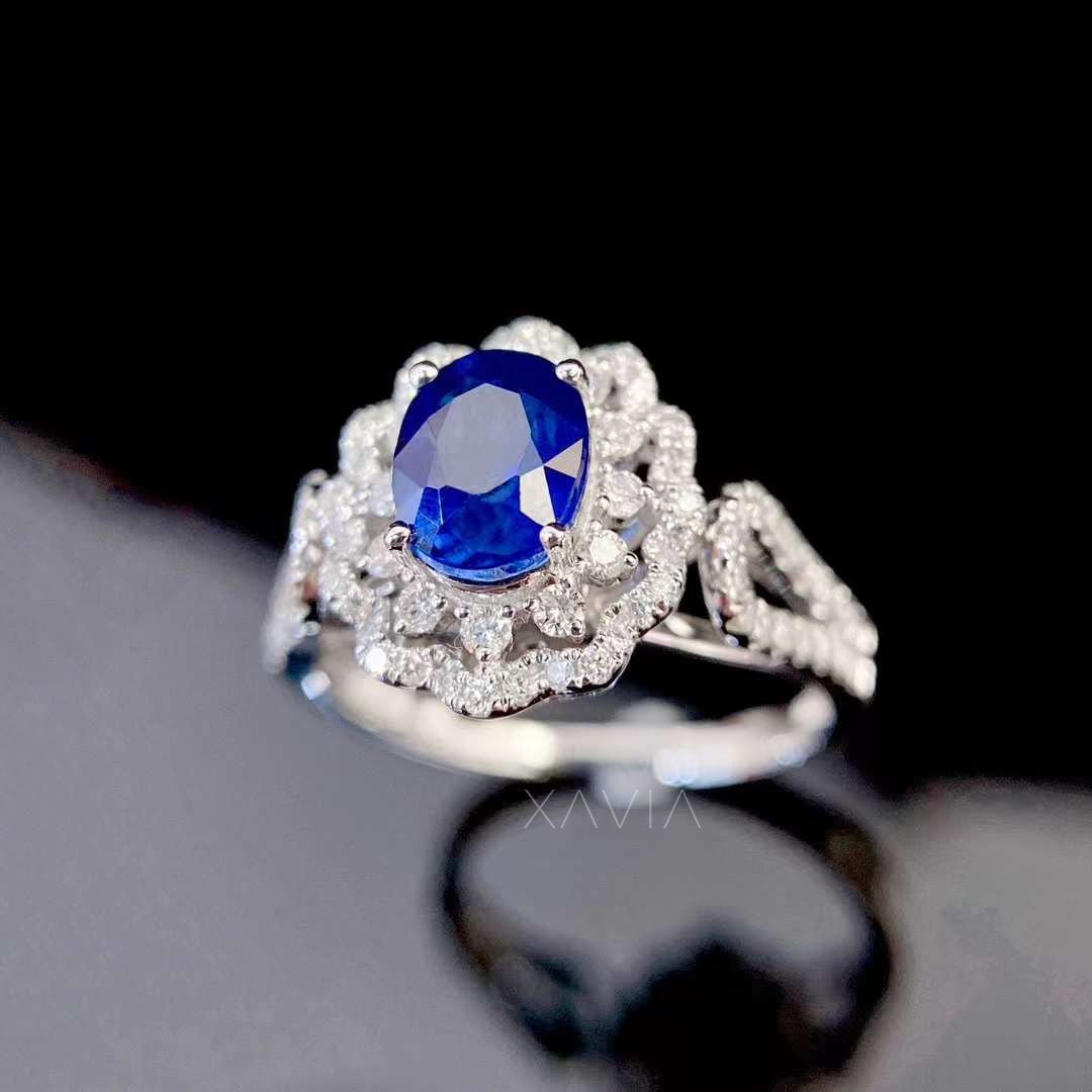 close up macro view of oval blue sapphire center stone surrounded by brilliant round diamond floral halo with split pavé band luxury engagement ring