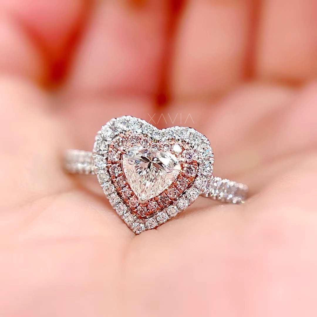 Close-up of heart-shaped lab-grown diamond ring with pink pavé inner halo and outer white diamond halo on pavé band in hand view