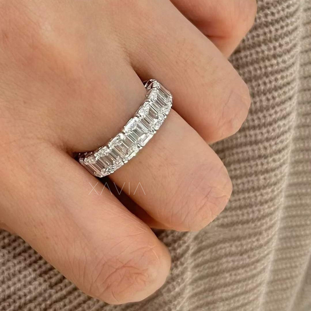 Emerald-cut diamond eternity ring in white gold, worn on finger with natural light reflecting each step-cut facet against soft knitwear.