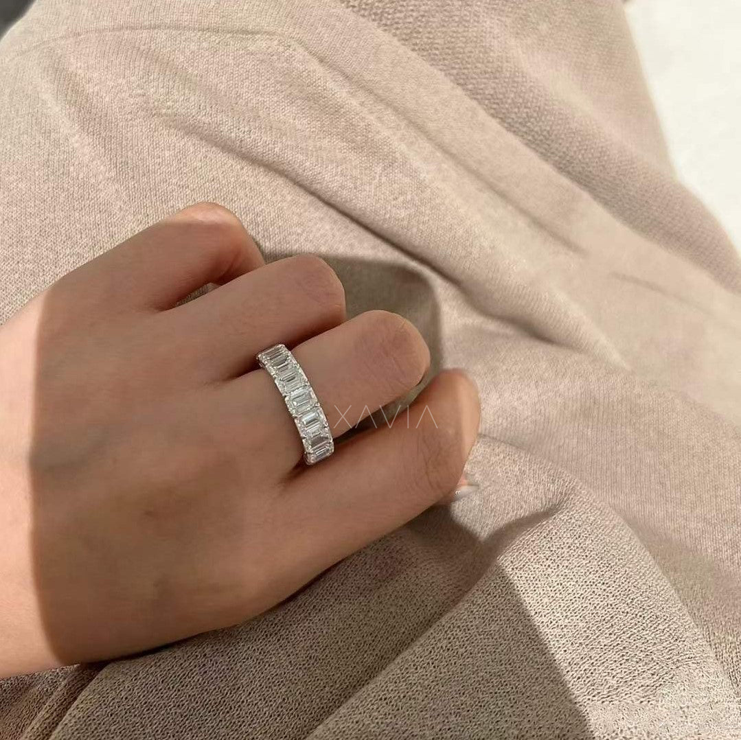 Side angle view of the emerald-cut diamond ring resting on neutral beige fabric, revealing shared prong craftsmanship and fluid brilliance.