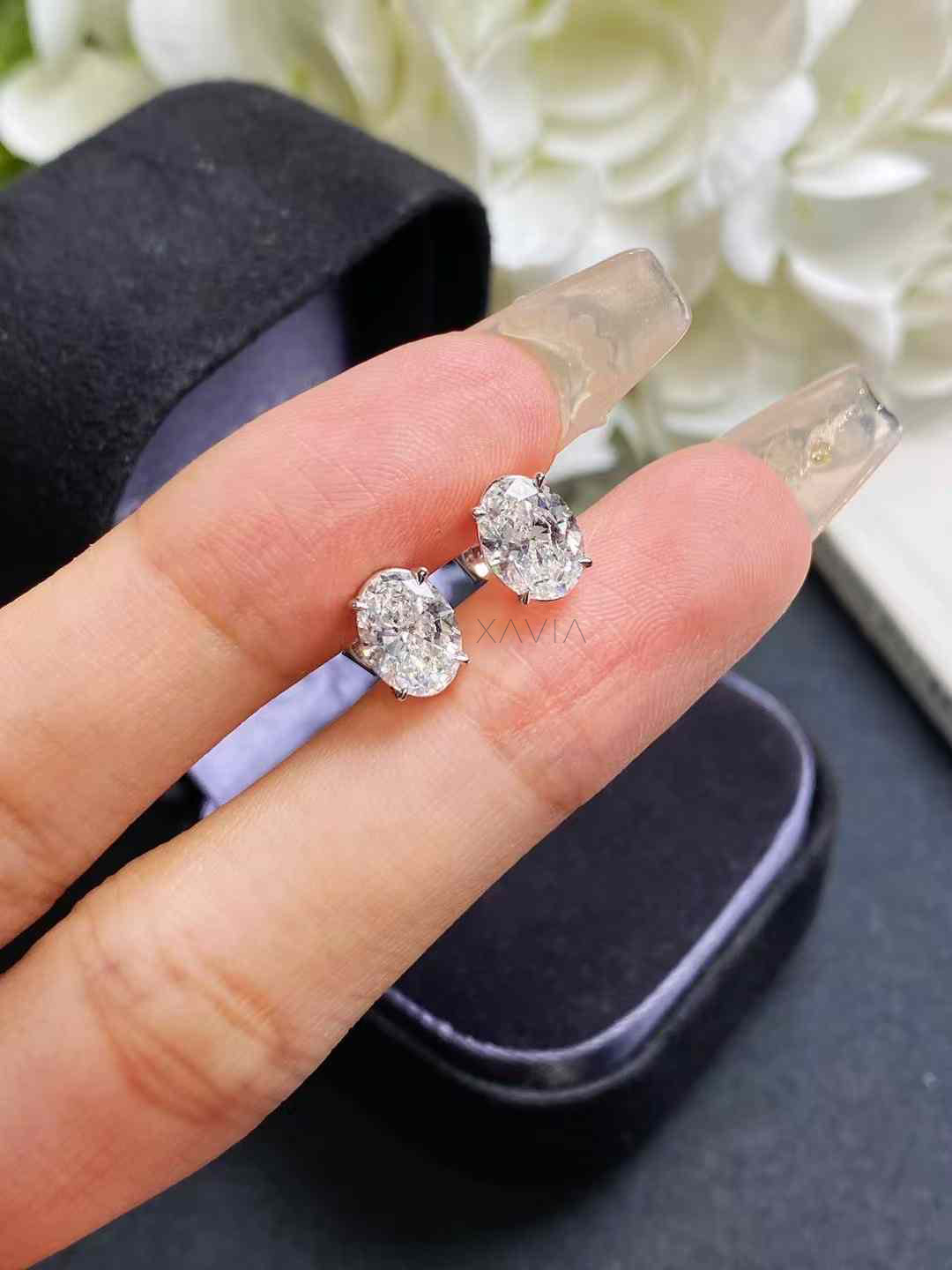 Close-up view of oval lab diamond studs on fingers with black box