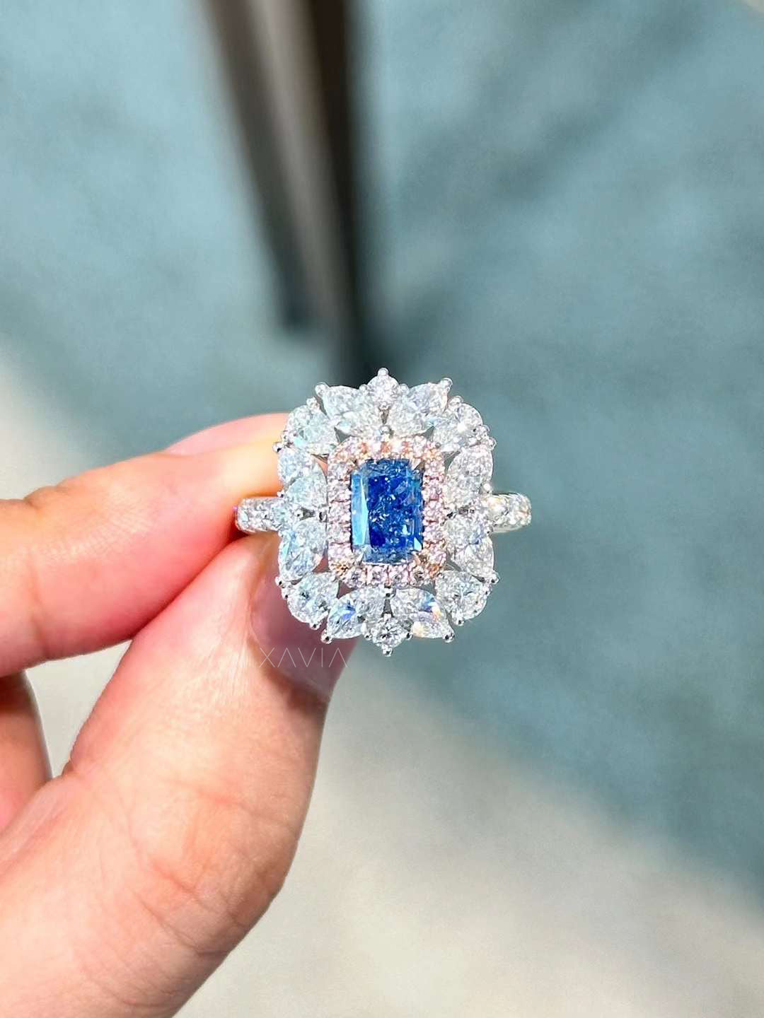 statement emerald cut blue lab diamond ring with double halo of marquise and round diamonds held in hand