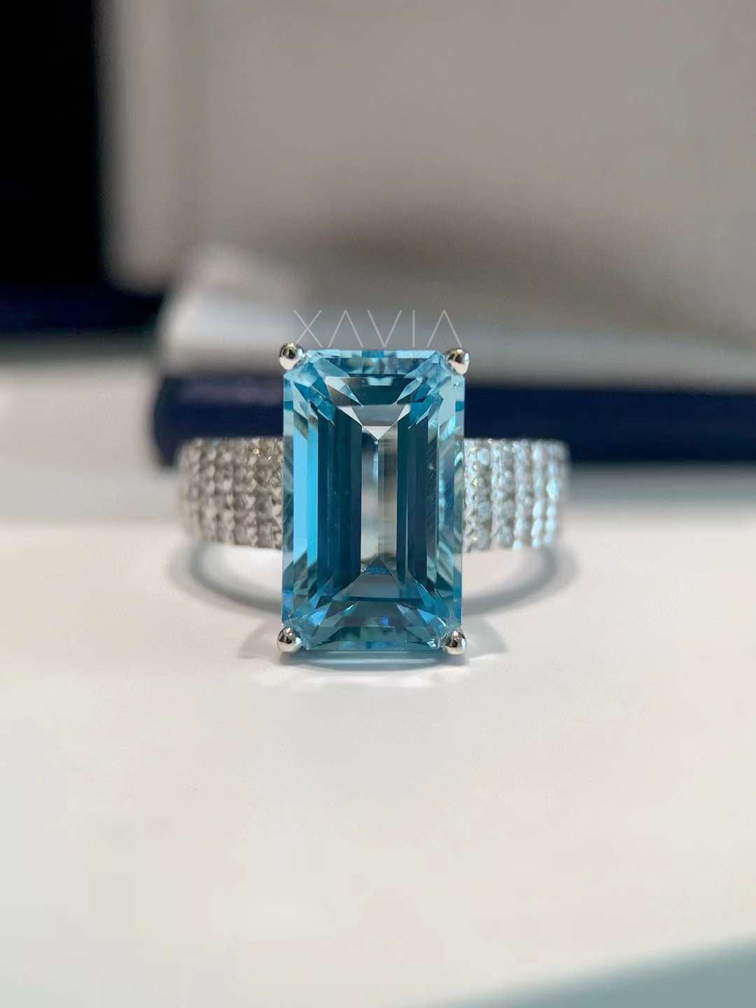 Front view of emerald cut sky blue gemstone cocktail ring with pavé diamond band in white gold, photographed under studio lighting