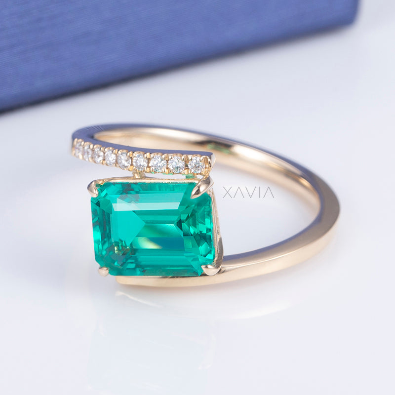 Side profile showcasing emerald cut lab diamond elevated prong setting with pavé curved accent on open gold band
