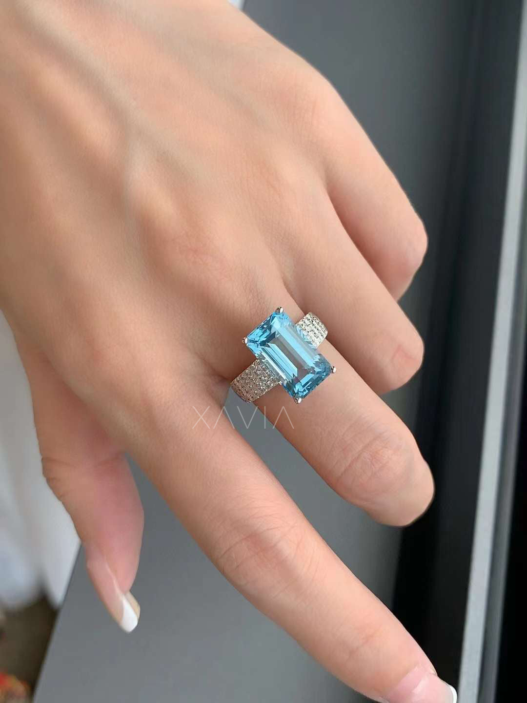 Emerald cut blue gemstone cocktail ring with pavé diamonds in white gold worn on model’s hand for scale and luxury styling