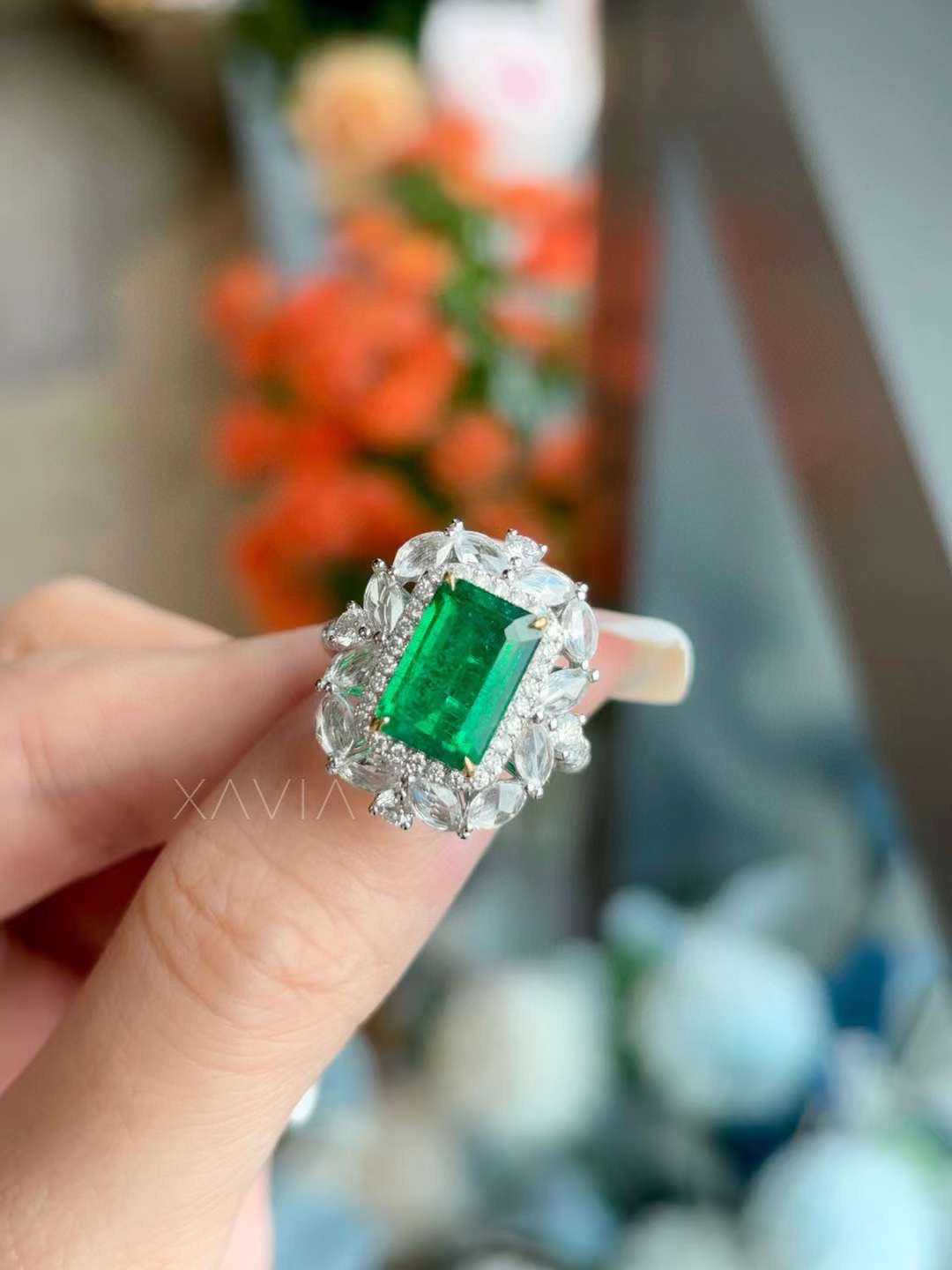 Close-up view of emerald cut vivid green gemstone cocktail ring surrounded by marquise and round lab grown diamond floral halo set in polished white metal