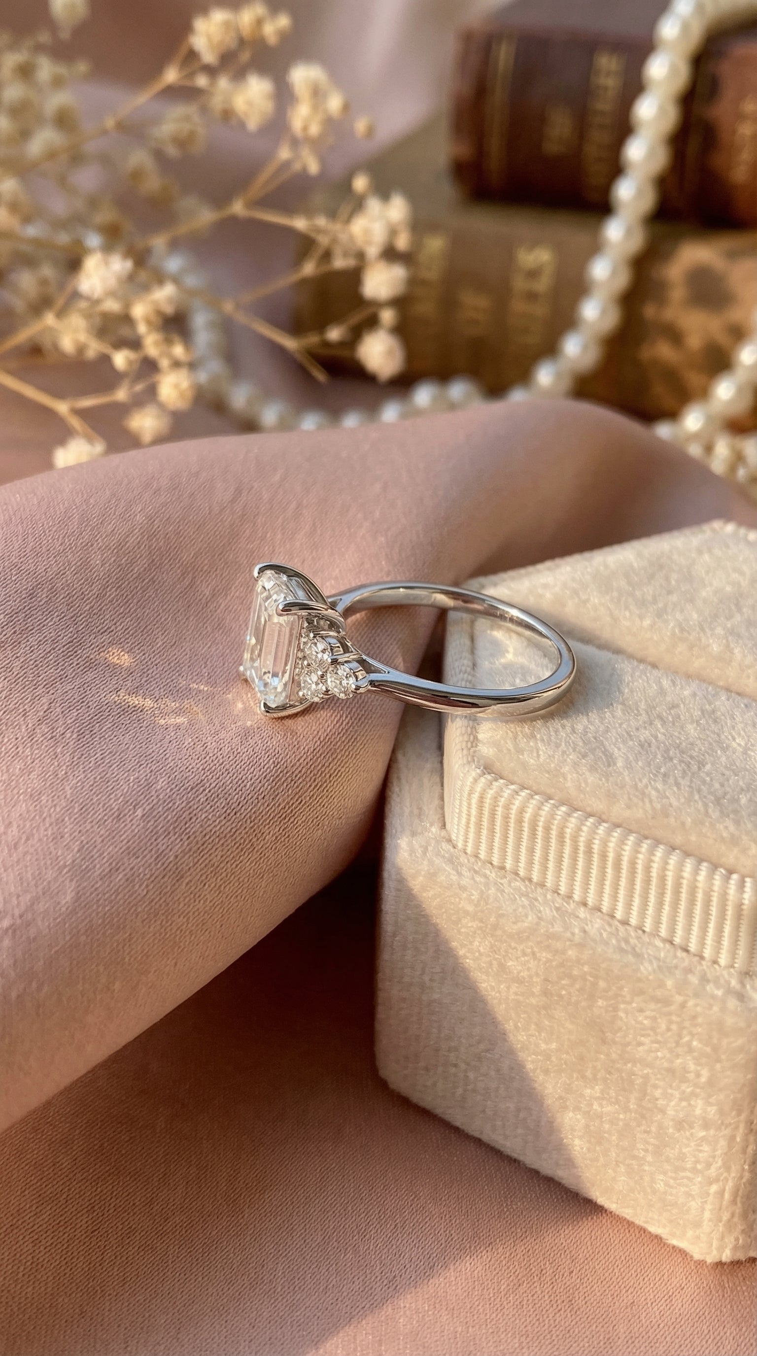 Side angle view of emerald cut lab grown diamond engagement ring featuring cluster round side diamonds set in a delicate prong setting on polished white gold band.