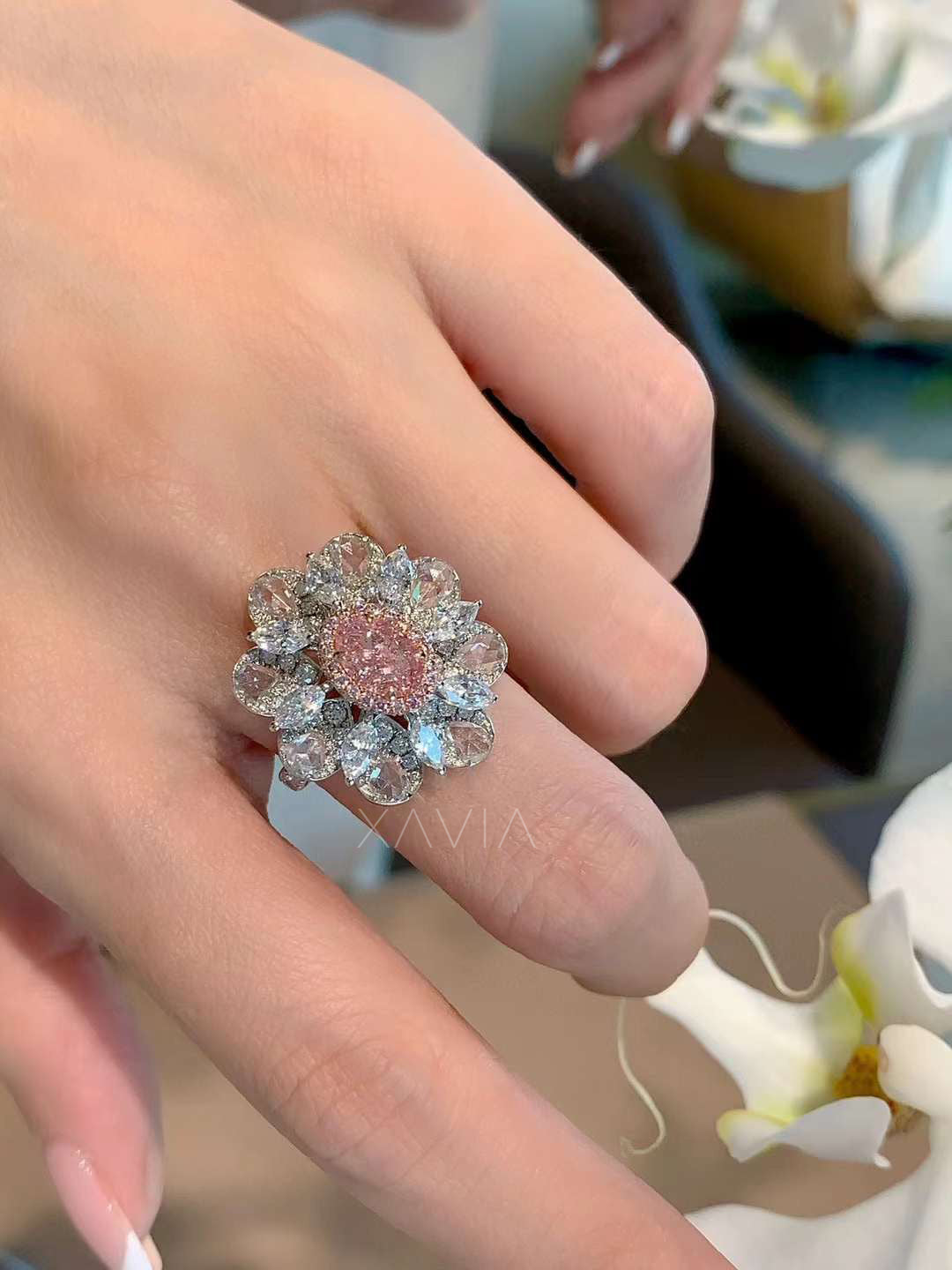 large floral cocktail ring with pink oval diamond worn on woman's finger, surrounded by orchids