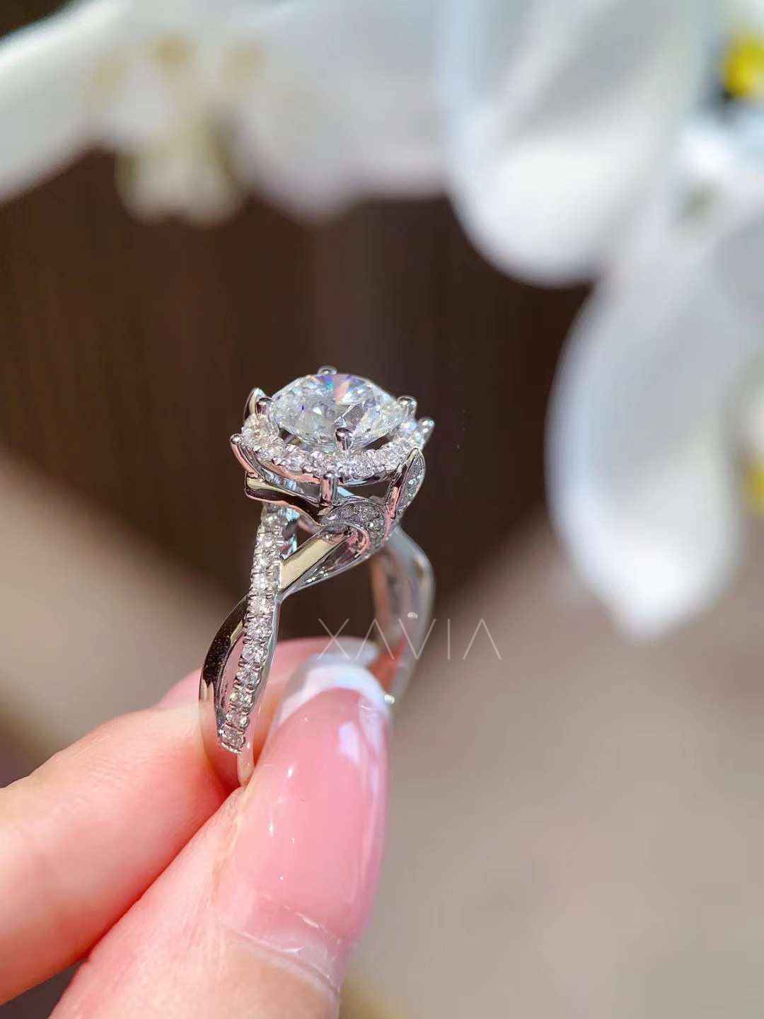 Lab-grown diamond round halo engagement ring worn on hand, showing twisted pavé band and petal-inspired cathedral setting with white orchids