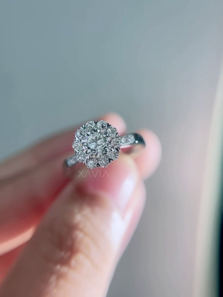 Close-up top angle of round diamond engagement ring featuring floral halo cluster of accent diamonds and polished white gold pavé shank