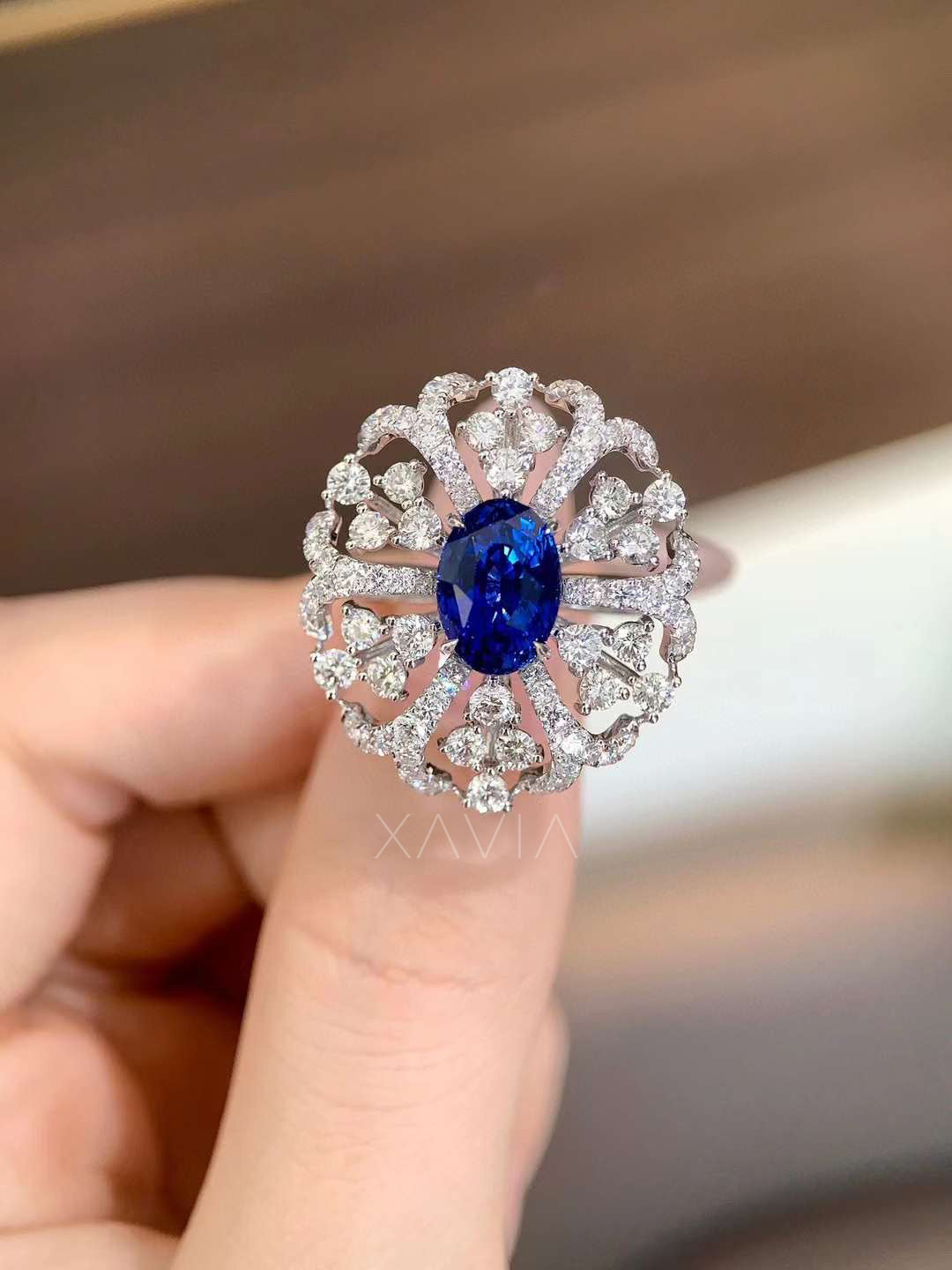 Top angle of oval blue gemstone ring featuring clustered round lab diamonds arranged in a sculptural floral halo design