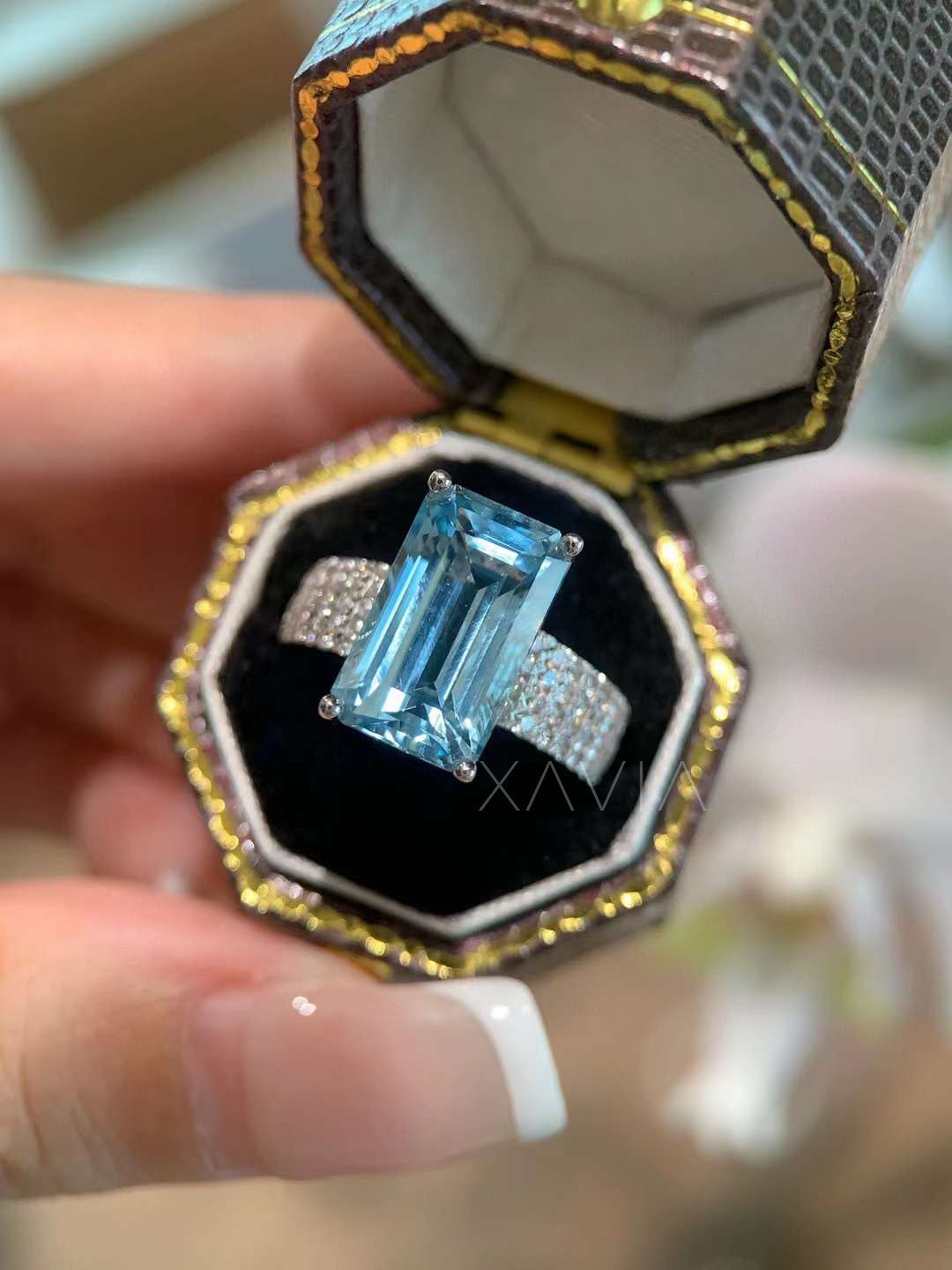 Emerald cut blue gemstone statement ring with pavé diamond band presented in luxury jewelry box