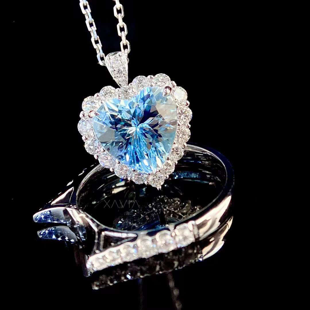 Luxury reflection shot of heart shaped blue gemstone engagement ring with round diamond halo and pavé band captured on glossy black surface