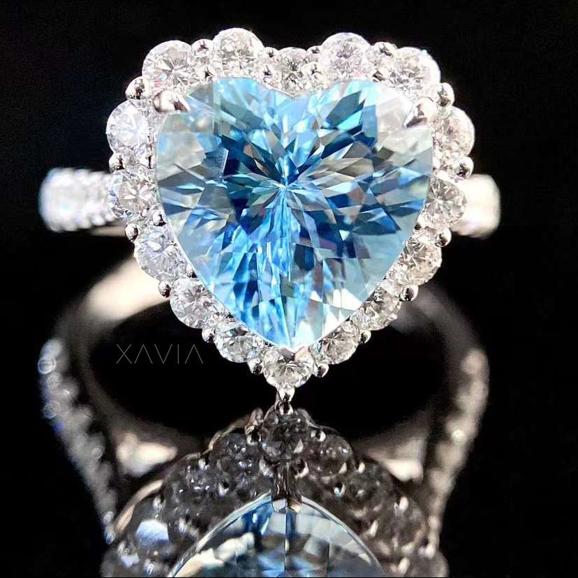 Close-up front view of heart cut ocean blue gemstone engagement ring surrounded by round brilliant lab diamond halo and pavé diamond band in white gold setting