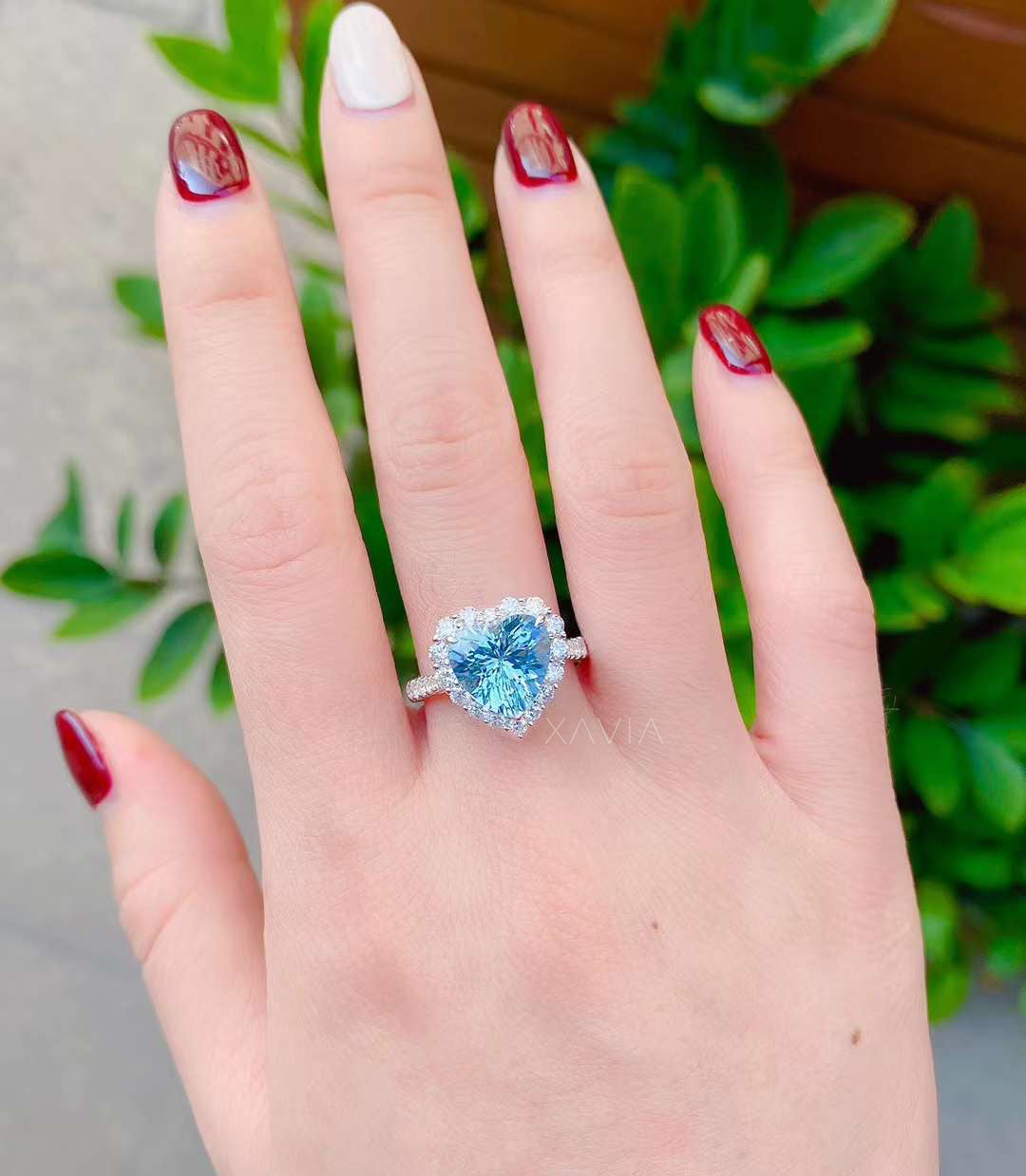 Heart shaped blue gemstone halo engagement ring worn on model hand showing pavé diamond band and sparkling round halo diamonds in solid white gold