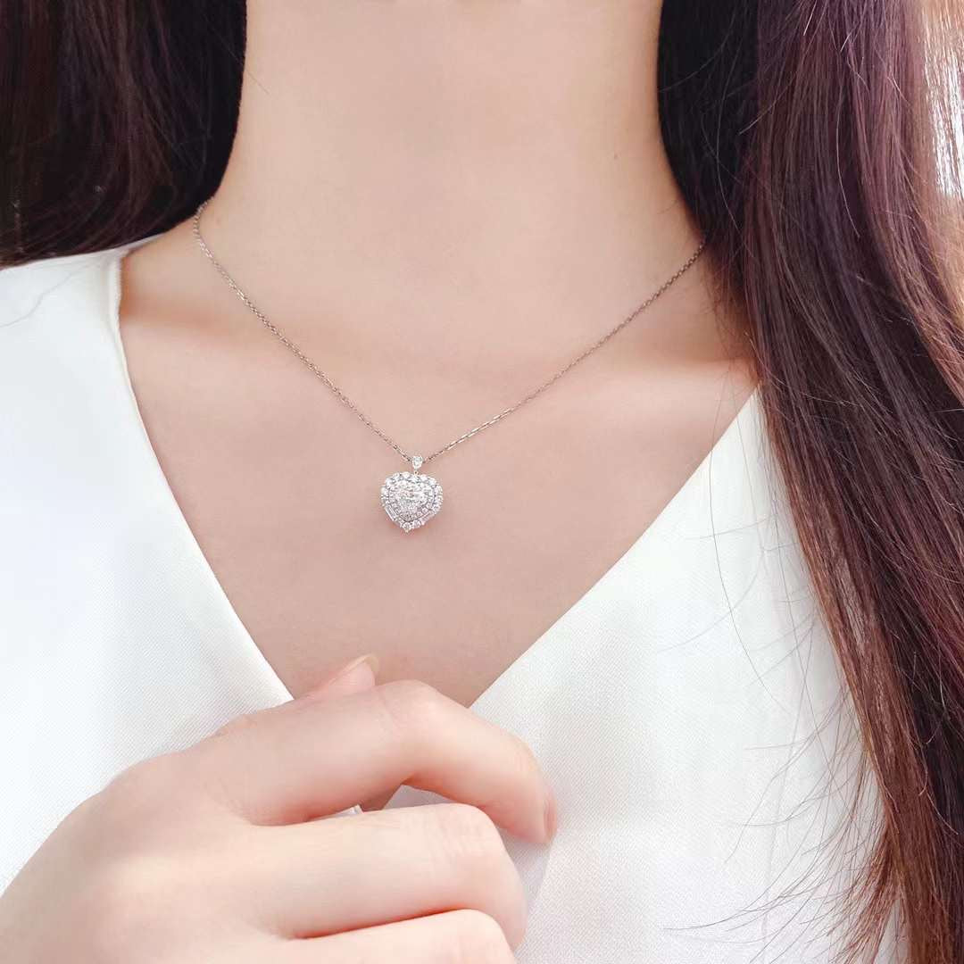 Elegant heart shaped diamond halo pendant necklace photographed on model chest highlighting brilliant center stone and sparkling halo diamonds
