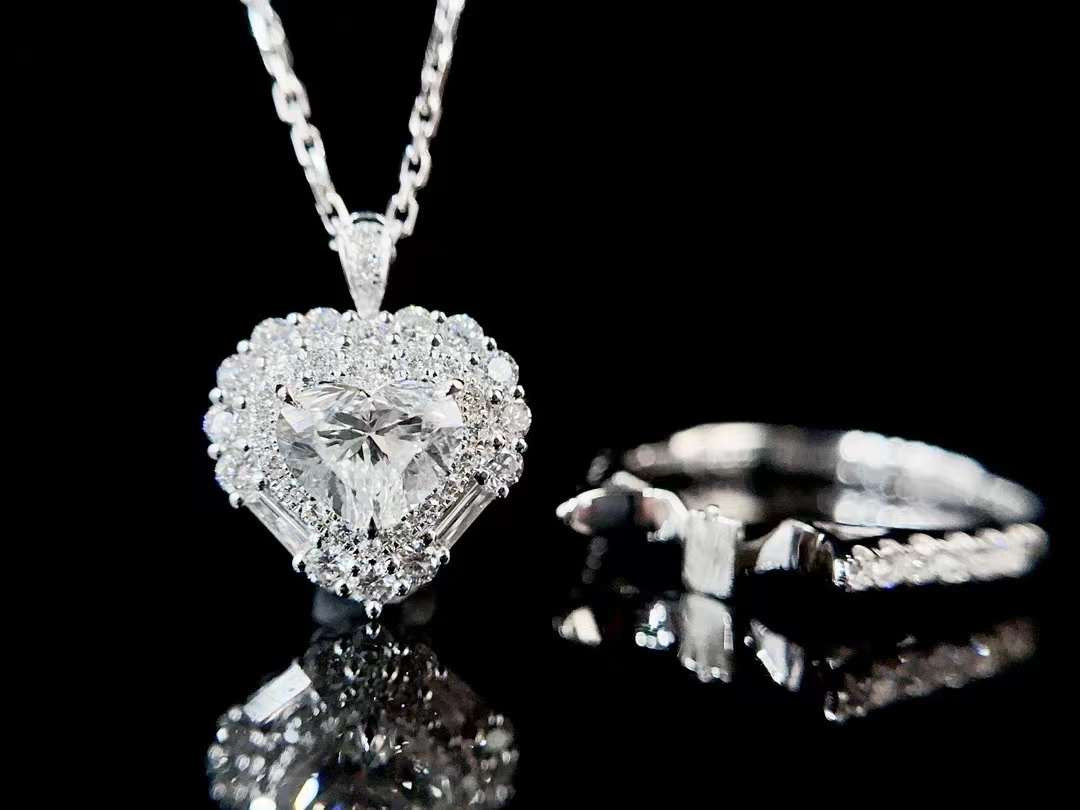 Studio image of heart cut diamond halo pendant and matching engagement ring showing brilliant halo diamonds, baguette accents and pavé band design