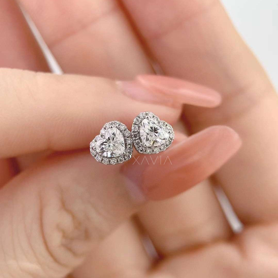 Heart-shaped diamond halo stud earrings in white gold displayed on silk