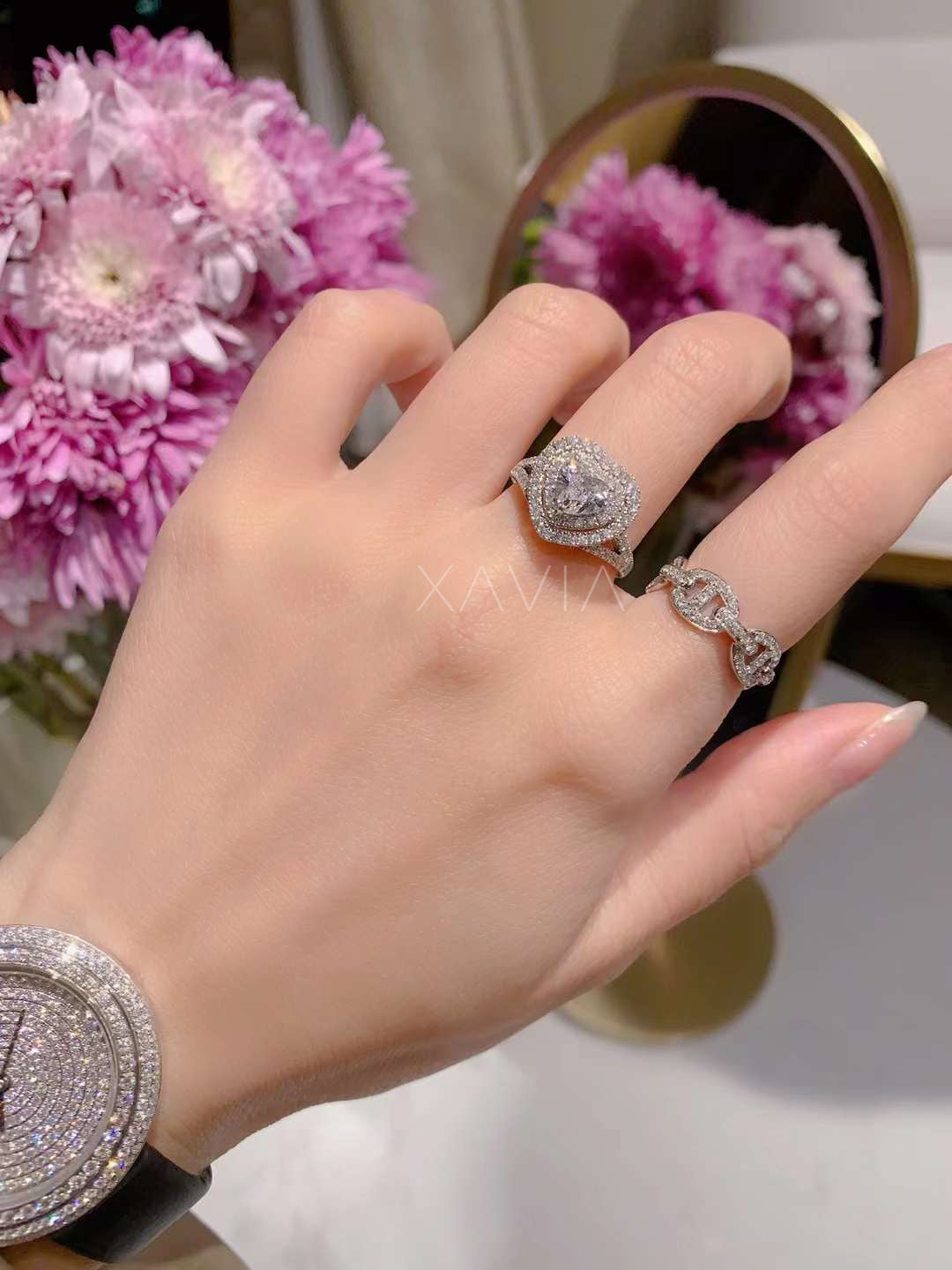 lifestyle image of model hand wearing heart cut diamond halo ring styled with diamond band and luxury watch