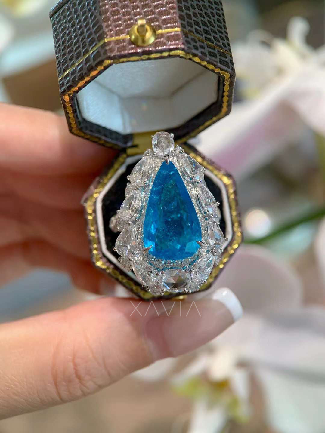 Close up of vivid blue pear gemstone ring surrounded by marquise oval and round lab grown diamonds forming dramatic statement halo cocktail ring design