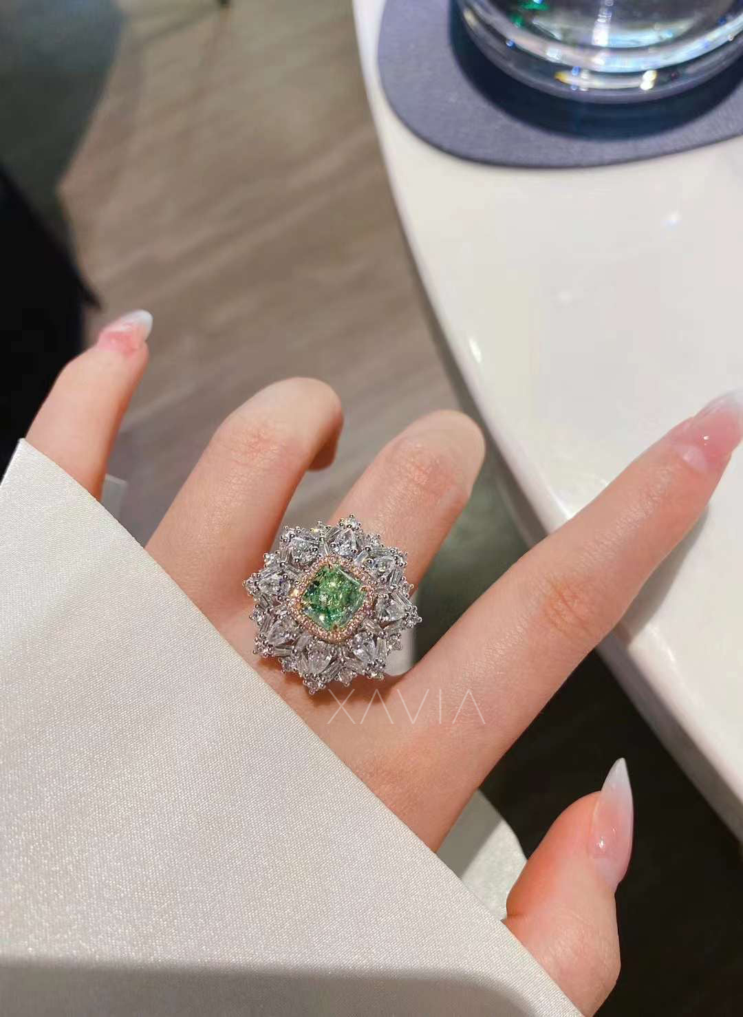model hand wearing cushion cut green diamond halo ring with pavé pink halo and clustered white diamond starburst