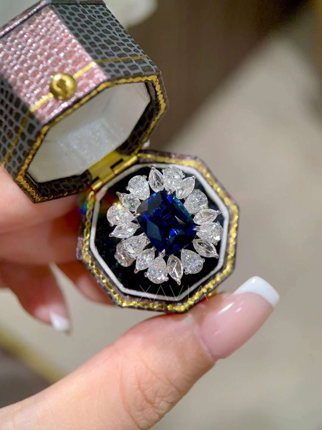 Top angle photograph of royal blue cushion cut sapphire statement ring with sparkling pear and marquise diamond halo forming a symmetrical flower inspired cluster