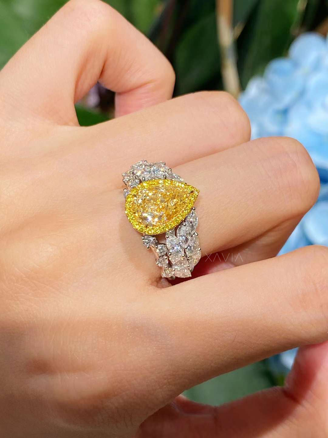 elegant platinum ring with fancy yellow pear cut diamond centerpiece, halo setting, and white diamond leaf band, shown on model’s hand