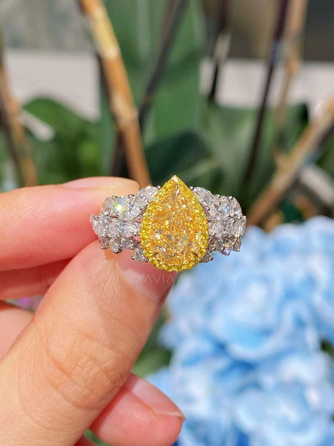 front angle of luxury platinum ring with fancy yellow pear cut diamond center, pavé halo, and white marquise diamond leaf band