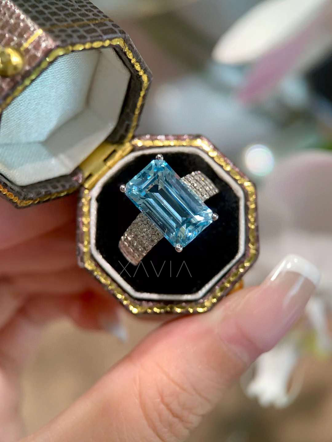 Angled top view of emerald cut sky blue gemstone cocktail ring with pavé diamonds on a wide band