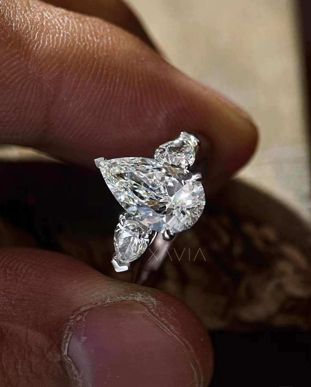 side profile of Novarae pear cut three-stone diamond engagement ring showing tapered side stones on high-polish band