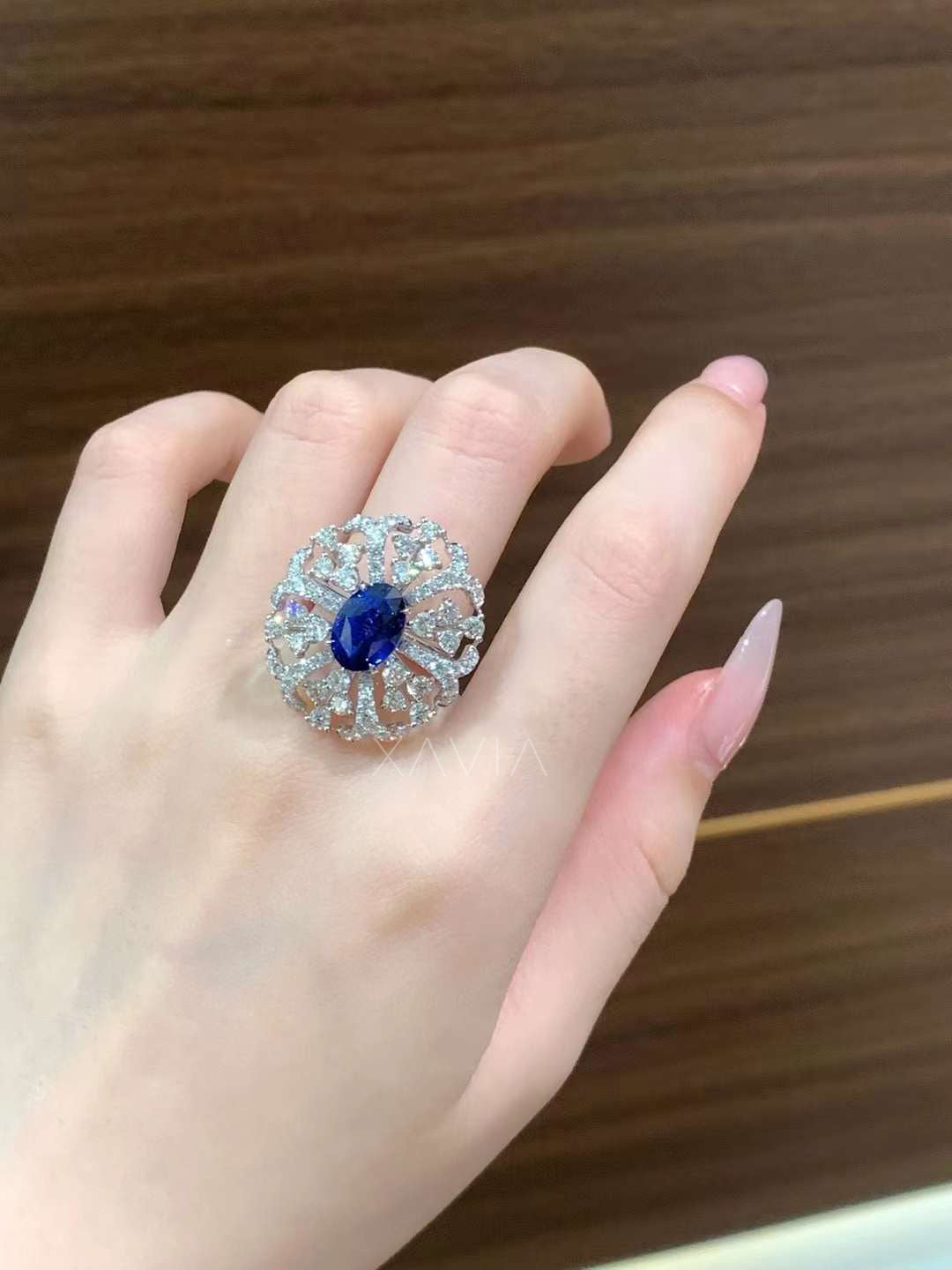 Oval blue center stone floral halo diamond ring worn on hand, showcasing bold cocktail scale and elegant brilliance