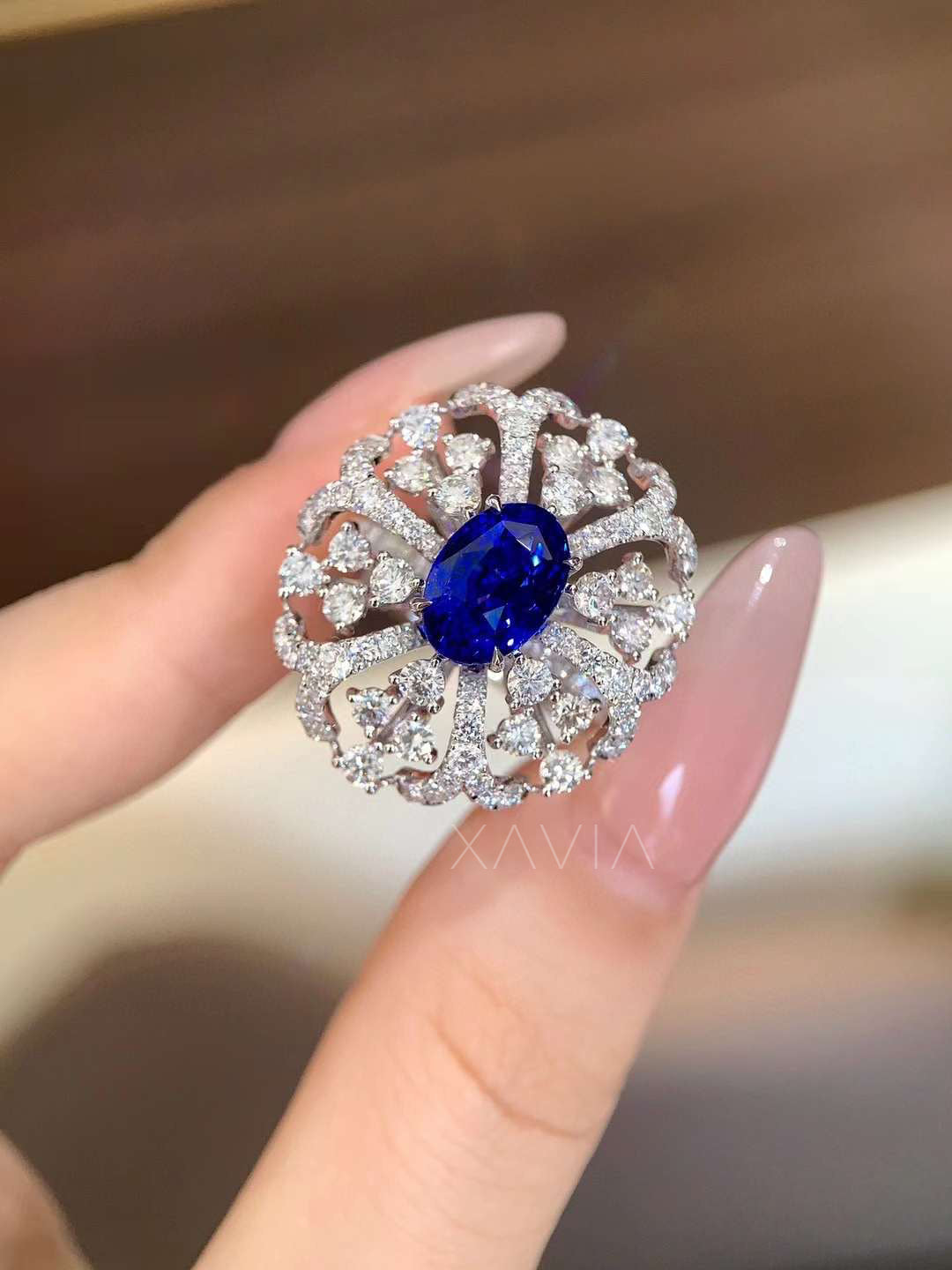 Close-up view of oval blue center stone ring with intricate floral halo of lab-grown diamonds in high-polish white gold setting