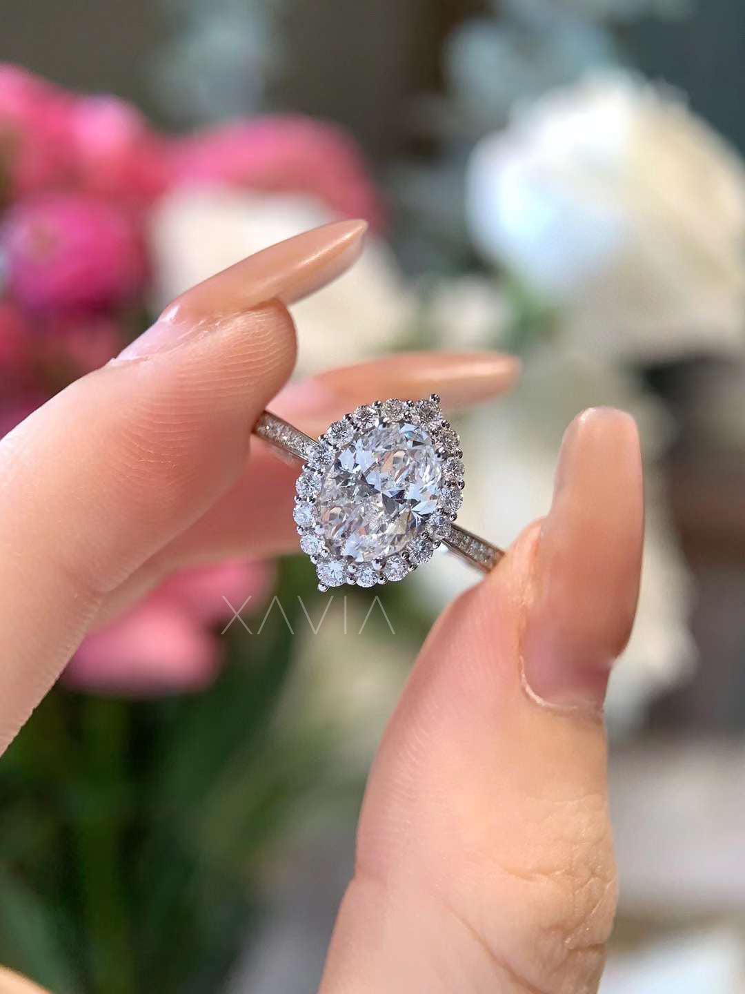 Oval cut lab grown diamond engagement ring worn on hand, featuring a floral halo design and pavé band in polished white gold