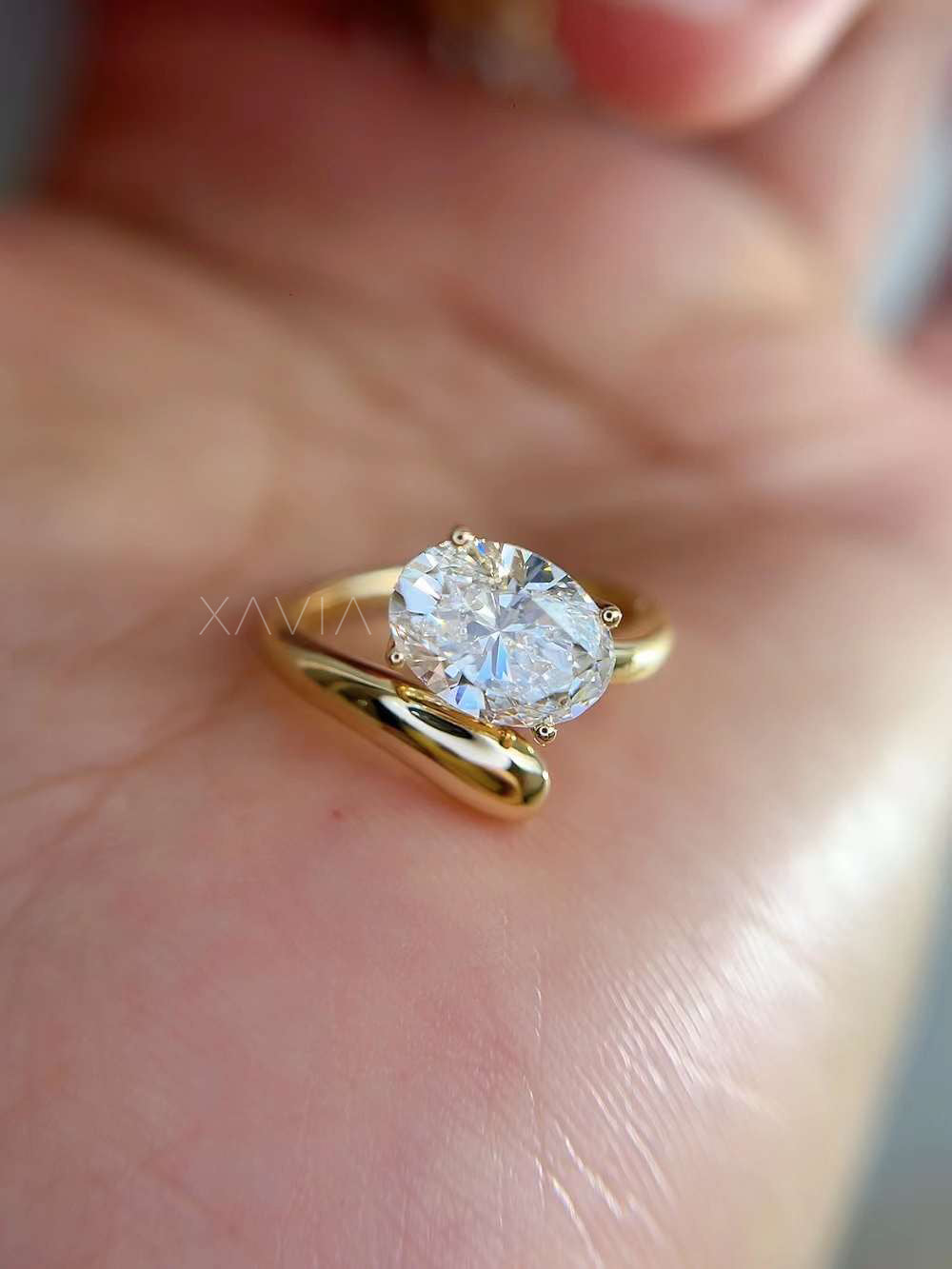 close-up of oval cut lab-grown diamond open wrap solitaire ring in yellow gold, worn on model’s hand showing high polish finish and minimal setting