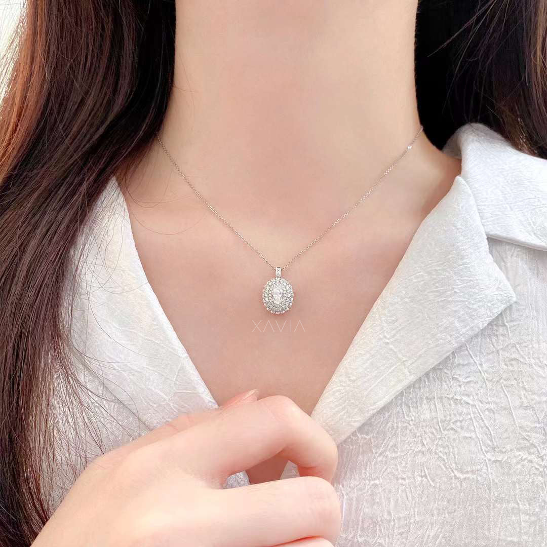 Silver necklace with a round pendant worn by a person against a white shirt background