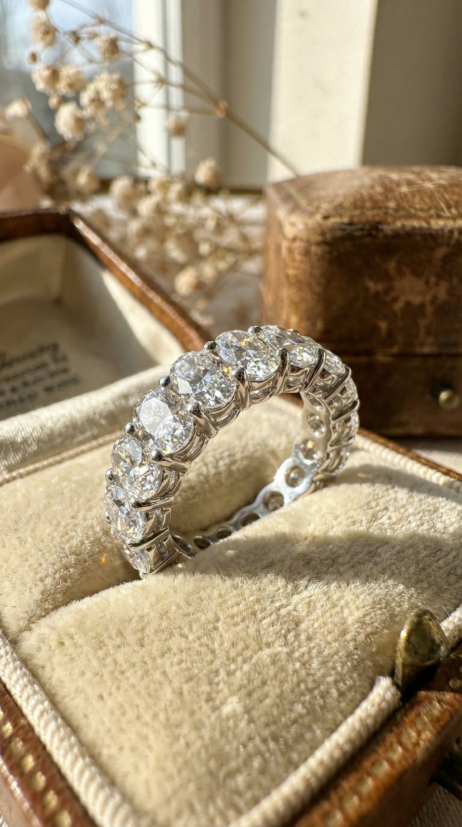 luxury oval cut lab grown diamond eternity band ring resting on champagne silk fabric highlighting brilliant diamonds and white gold setting