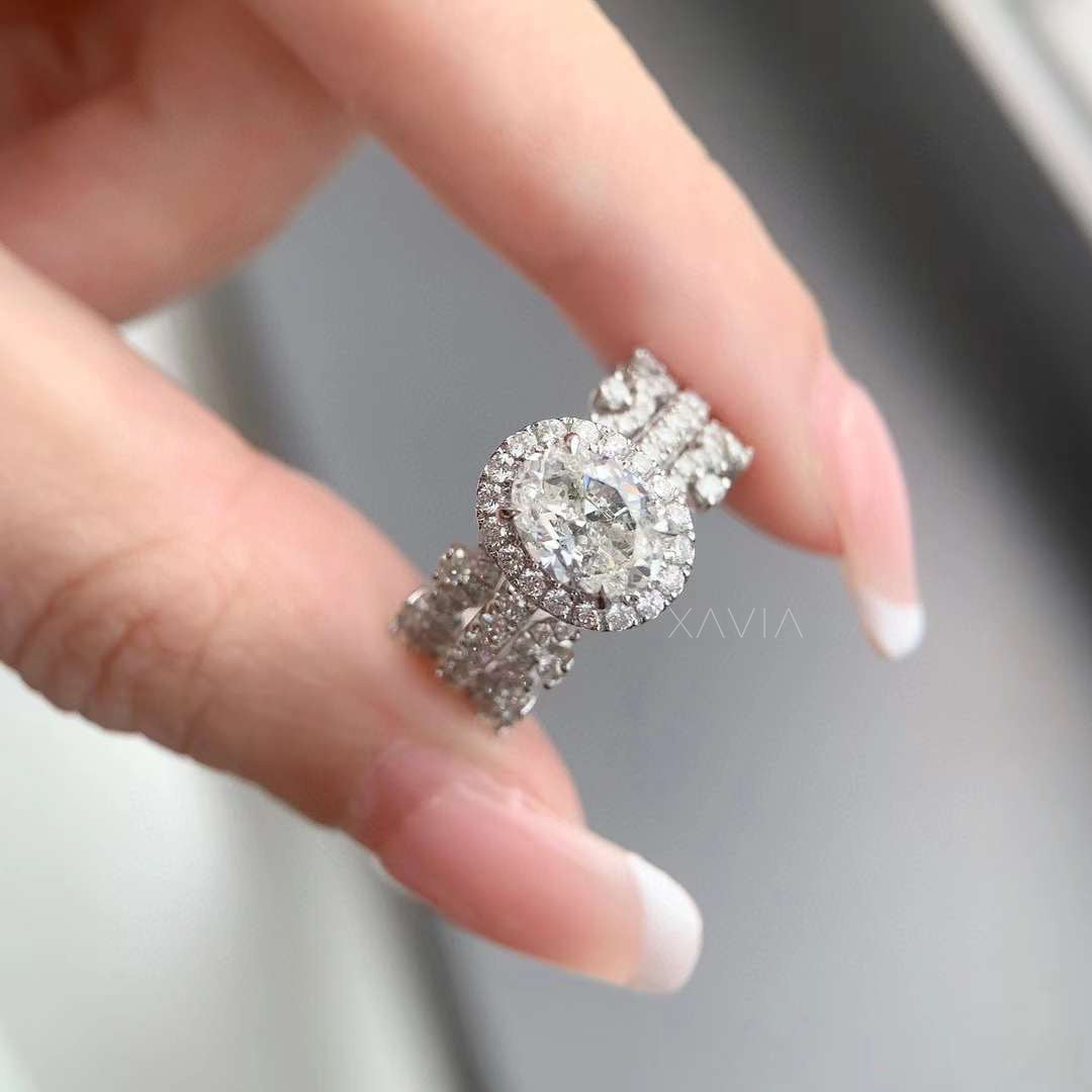 Close-up view of oval cut lab grown diamond halo engagement ring featuring round diamond halo and intricate triple pavé vine band held between fingers showing brilliant sparkle