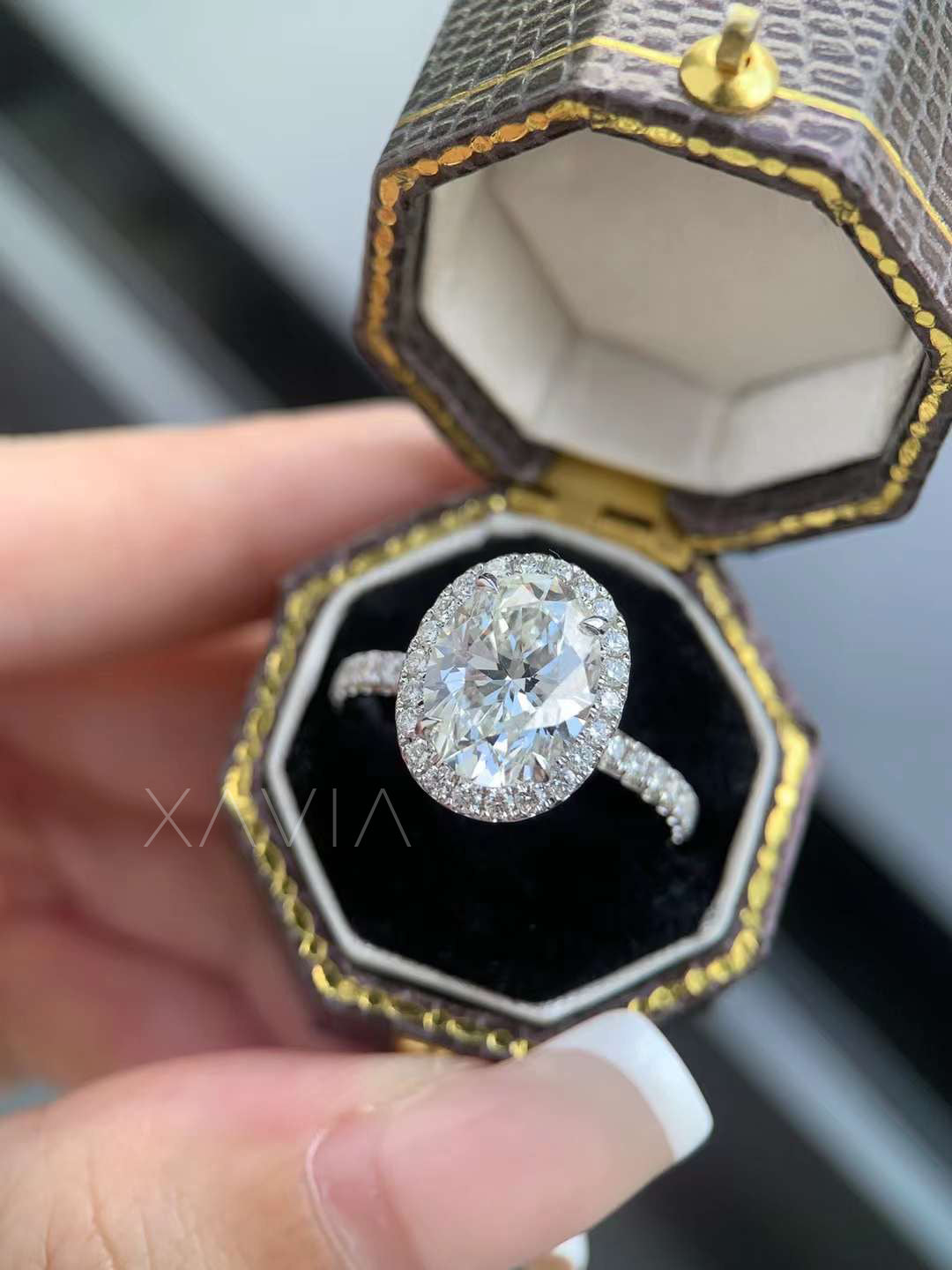 Oval cut halo lab diamond engagement ring with pavé shank, showcased in a black velvet and gold-trimmed ring box