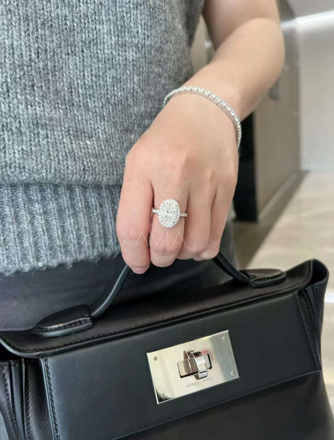 Lifestyle photo of oval halo lab-grown diamond engagement ring worn while holding designer handbag, modern luxury styling