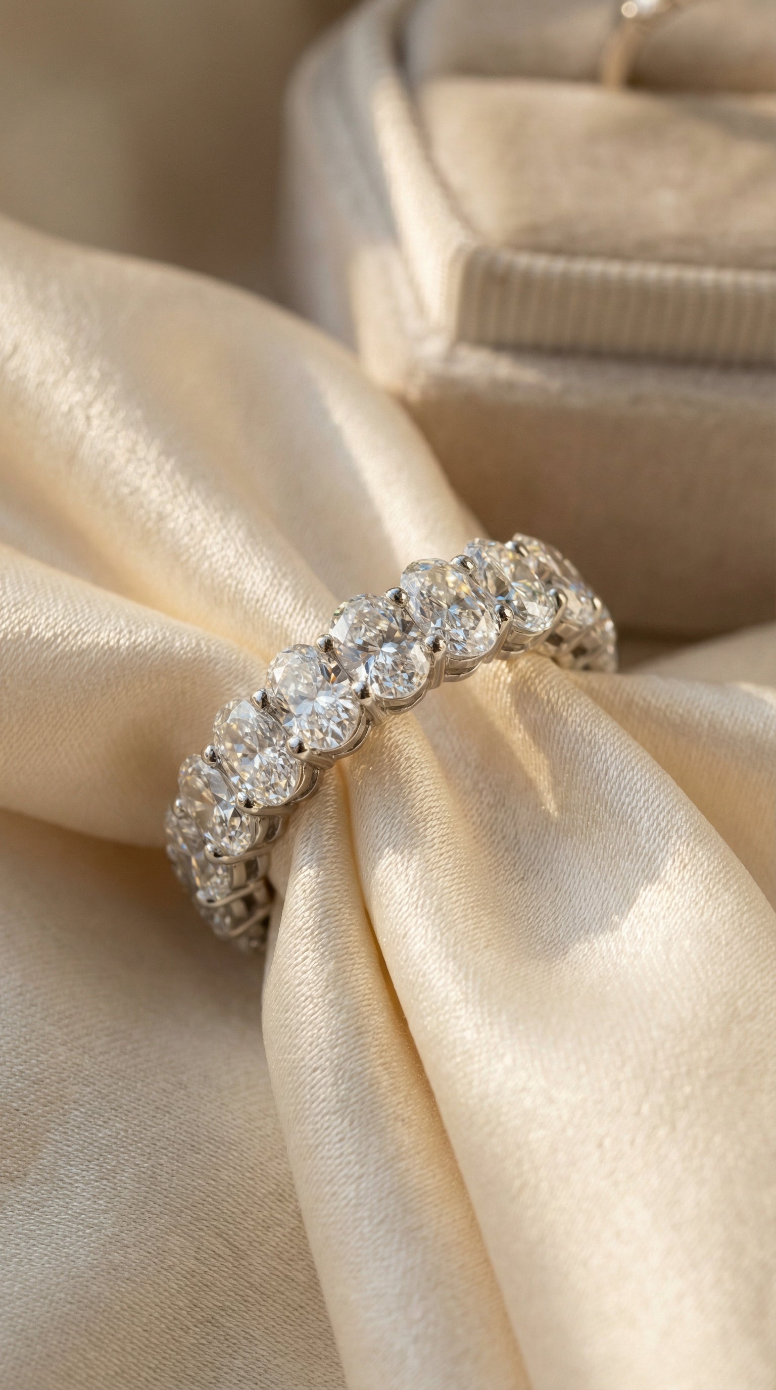 luxury oval cut lab grown diamond eternity band ring resting on champagne silk fabric highlighting brilliant diamonds and white gold setting