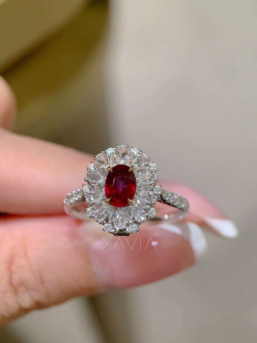 Elegant hand shot of oval red gemstone halo ring featuring marquise floral diamond halo and pavé diamond band demonstrating luxury scale and brilliance