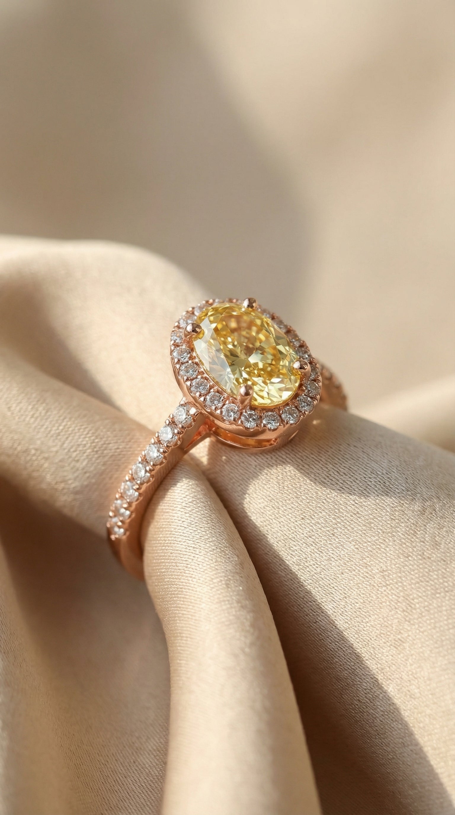 Oval yellow lab-grown diamond halo engagement ring in rose gold with pavé band displayed on silk fabric