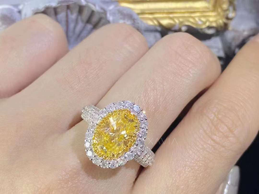 close-up of oval fancy vivid yellow diamond halo ring with pavé band worn on model’s hand, platinum setting